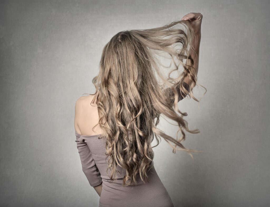 A stylish woman in an off-shoulder outfit, posing with wavy hair indoors.