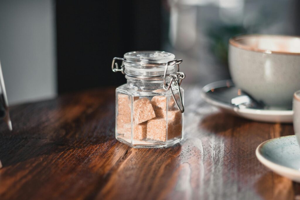 Warm cafe scene featuring a glass jar of brown sugar cubes on a wooden table.