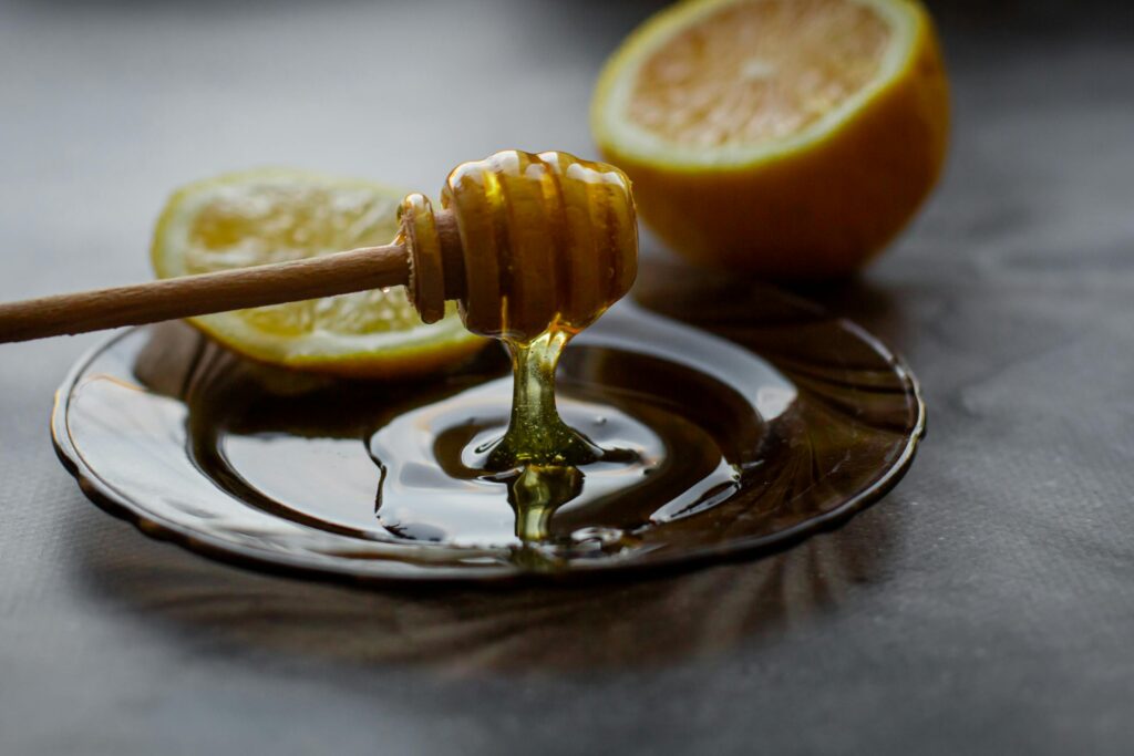 A close-up of a honey dipper with fresh lemon slices on a saucer, showcasing warm, natural lighting.